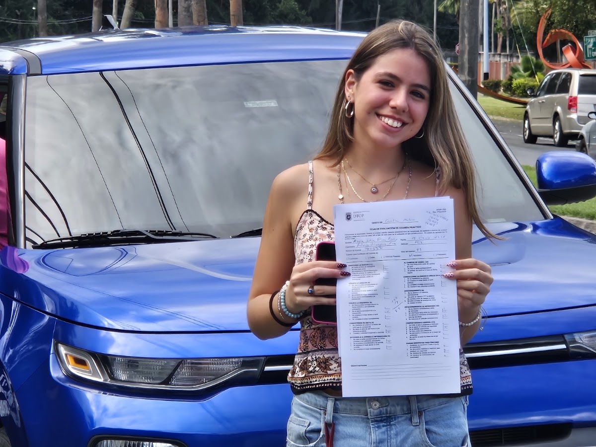 Estudiante aprobada frente al carro de la escuela