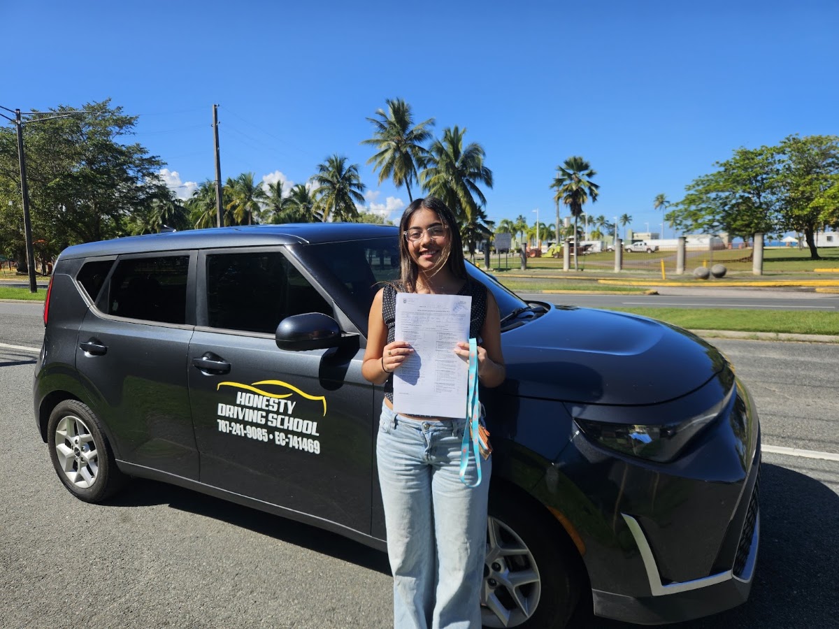 Estudiante con su hoja de examen aprobado frente al carro de Honesty Driving School