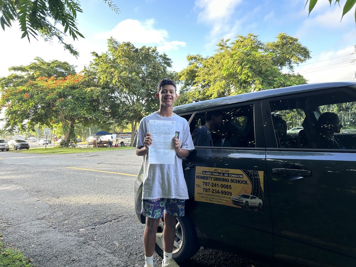 Estudiante aprobado junto al carro de la escuela